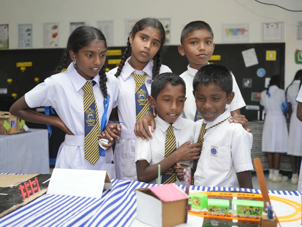Students stand beside the models they built, laid out on a table.