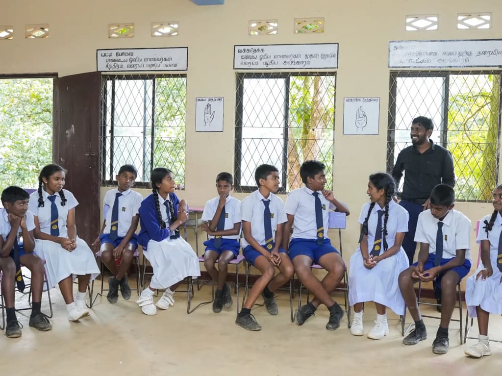 Students sit in a circle in a classroom with a facilitator.