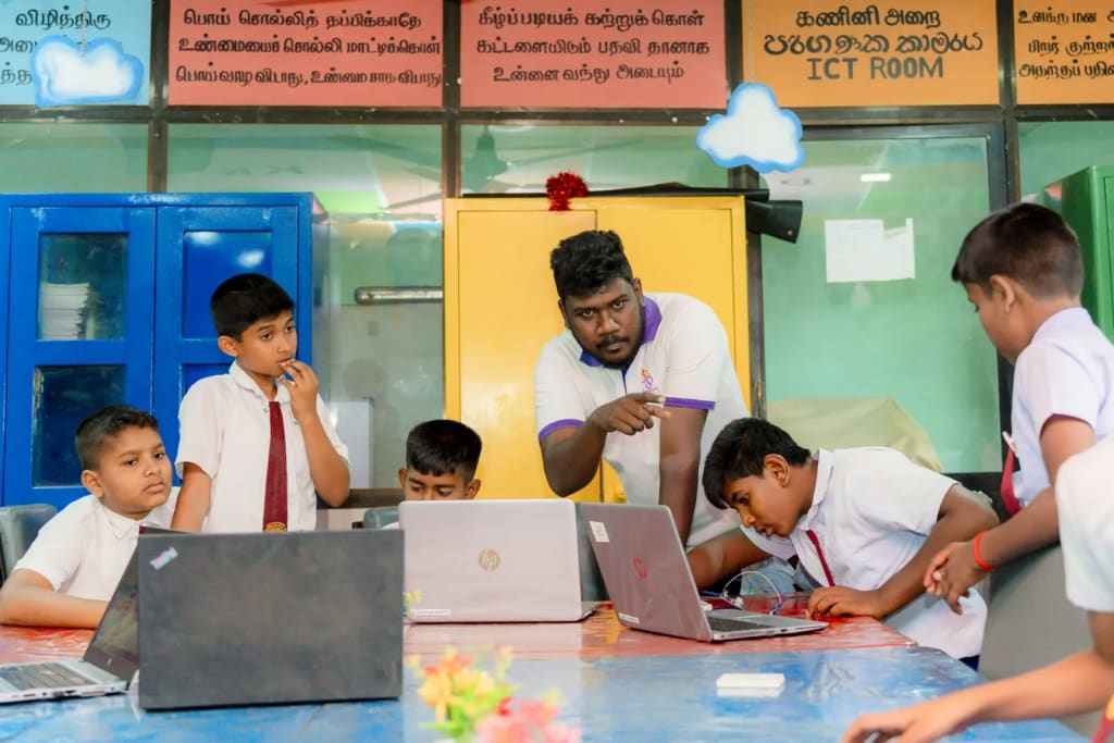 A trainer works with a group of students on electronics at their laptops.