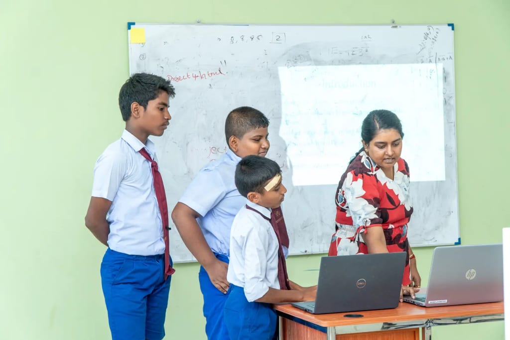 A group of students presents their work at the whiteboard with a facilitator.