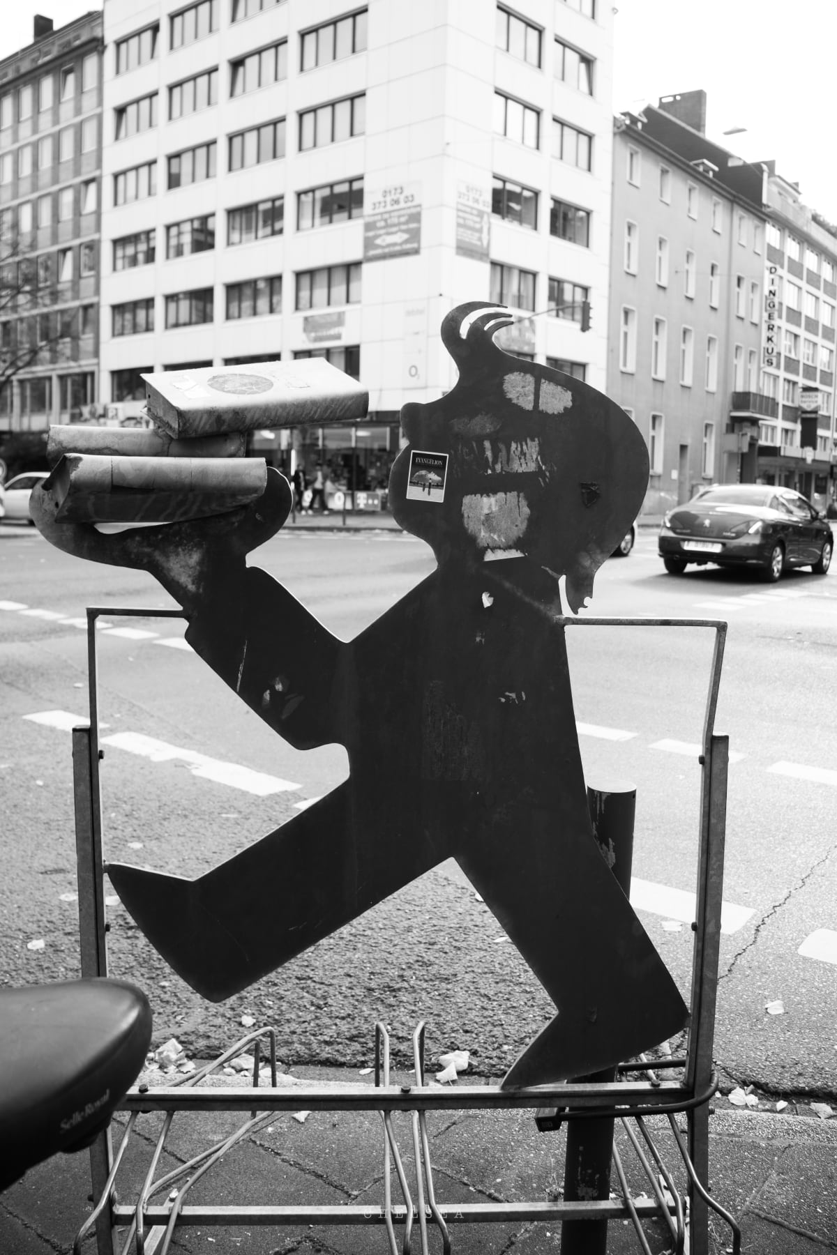 A black-and-white metal figure carrying a parcel beside a city street