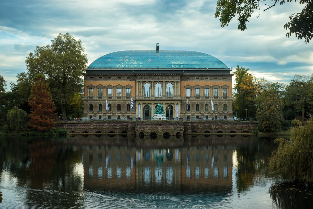 A historic museum reflected in a quiet pond beneath an overcast sky