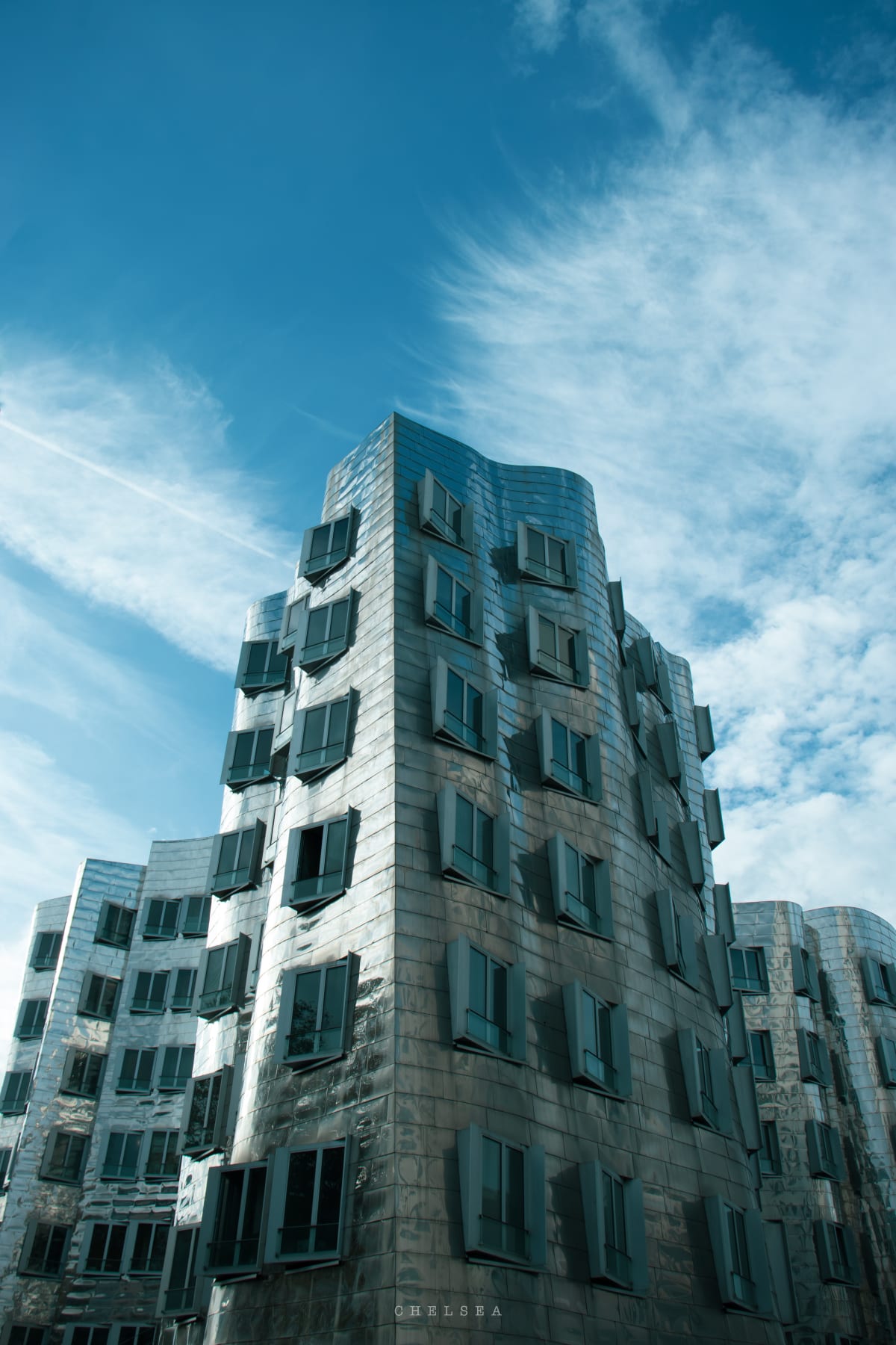 A curving metal-clad building beneath a bright blue sky