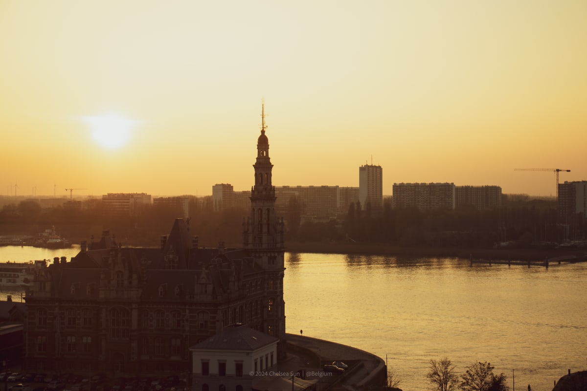 A historic riverside building silhouetted against a golden sunset