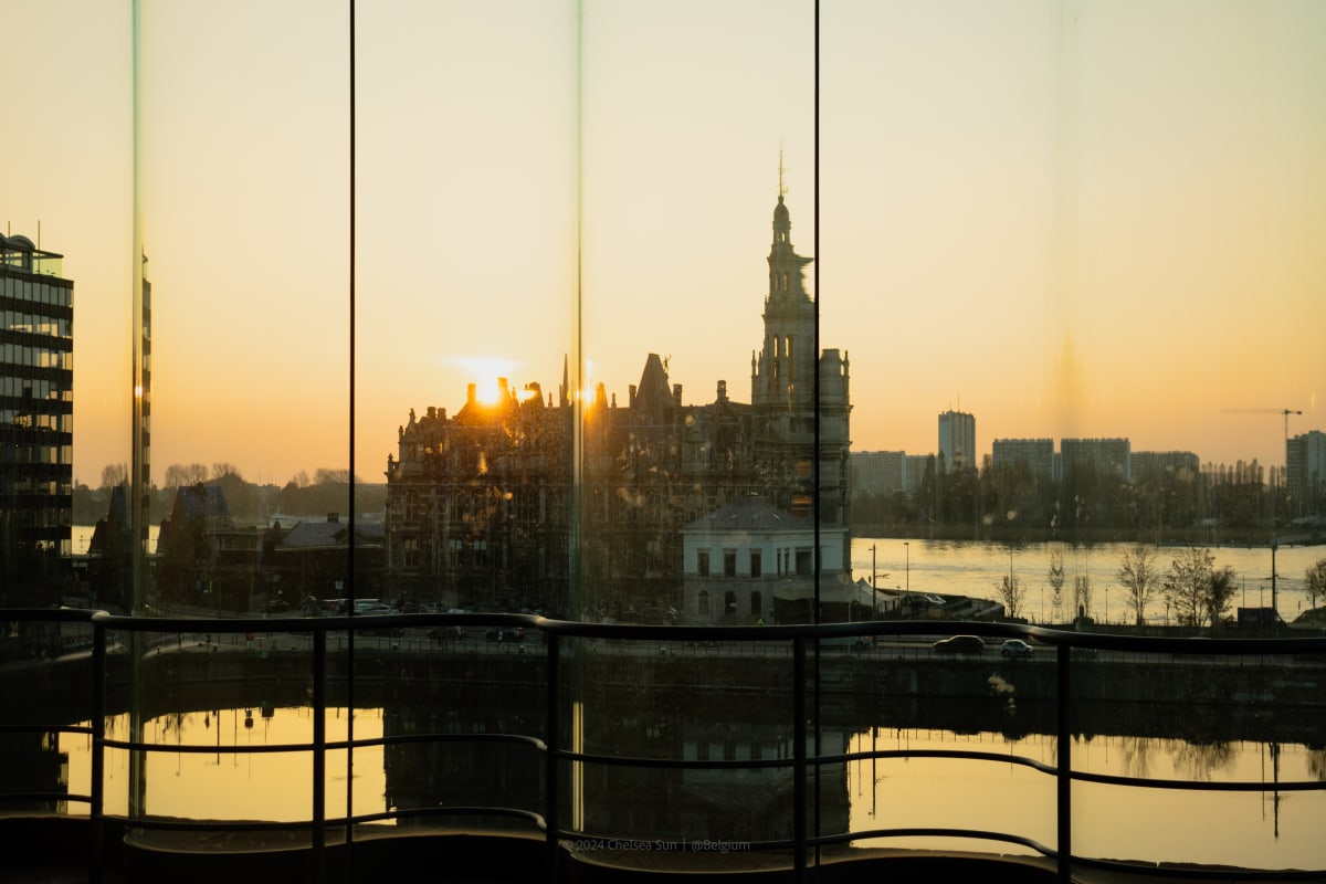 A riverside city skyline reflected across glass panels at sunset