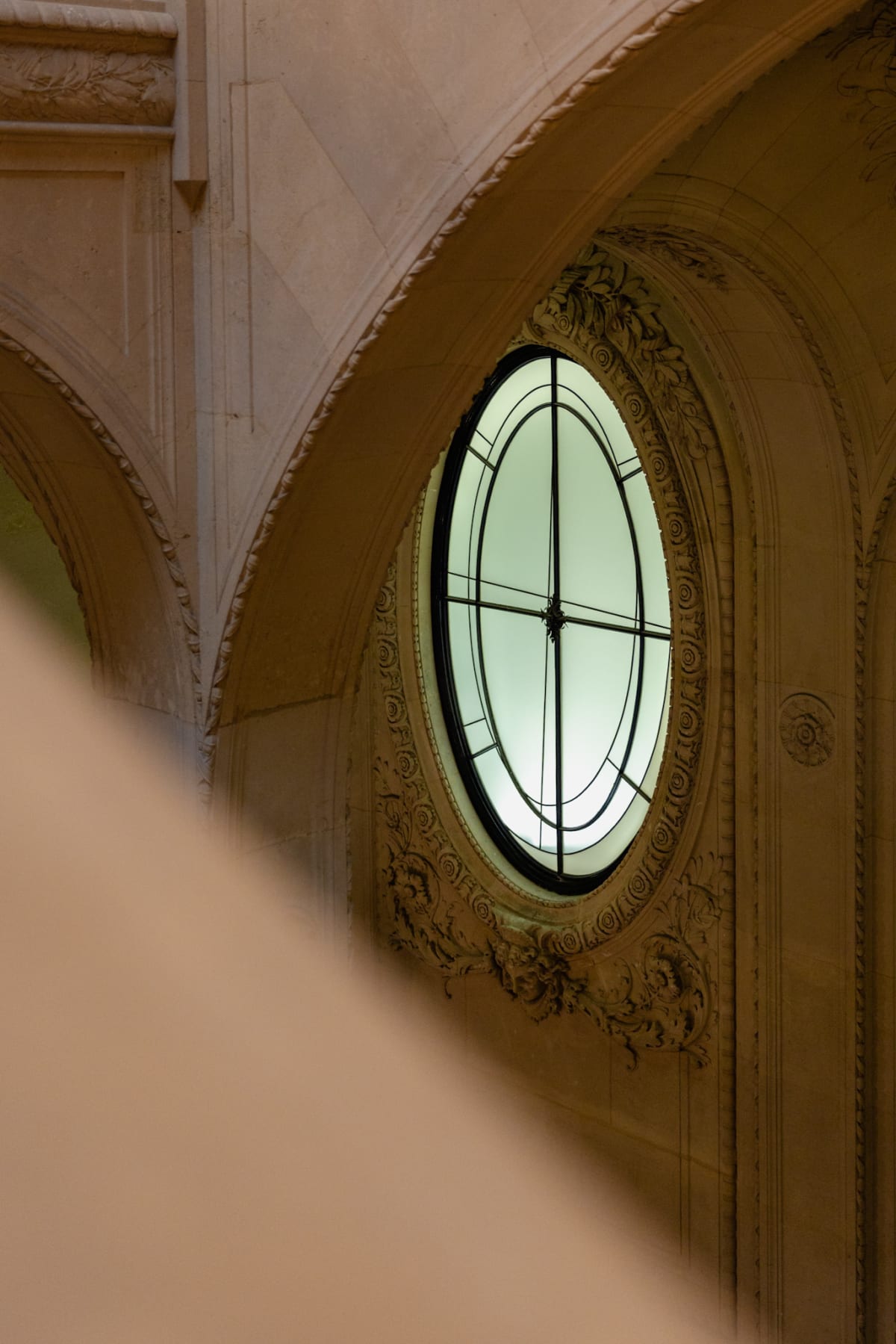 An oval window framed by ornate stonework inside the Louvre