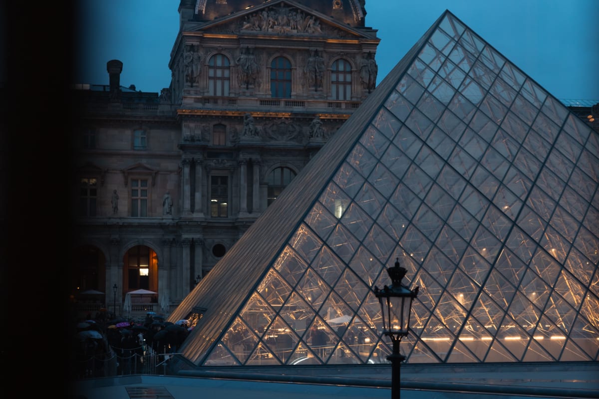 The Louvre Pyramid glowing against the palace at blue hour