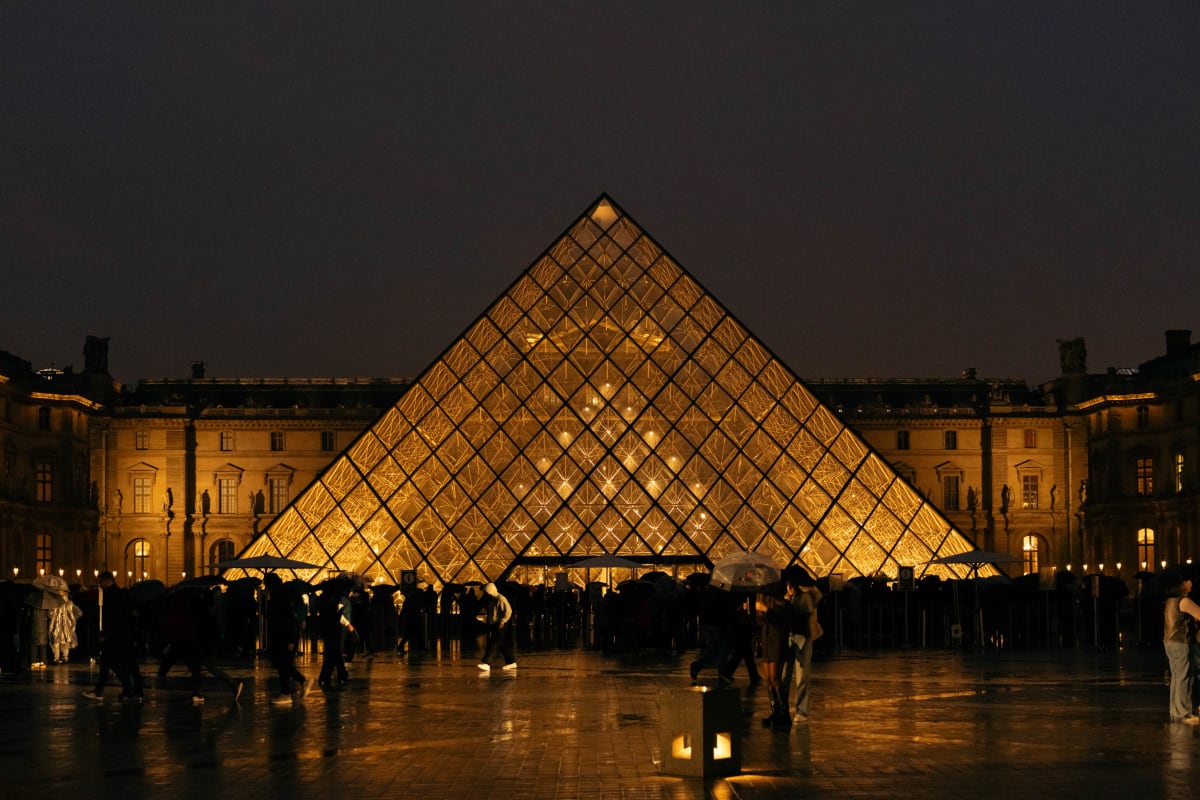 The illuminated Louvre Pyramid reflected on a rain-soaked courtyard