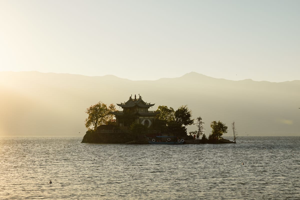 A small temple on an island across a lake in warm morning light