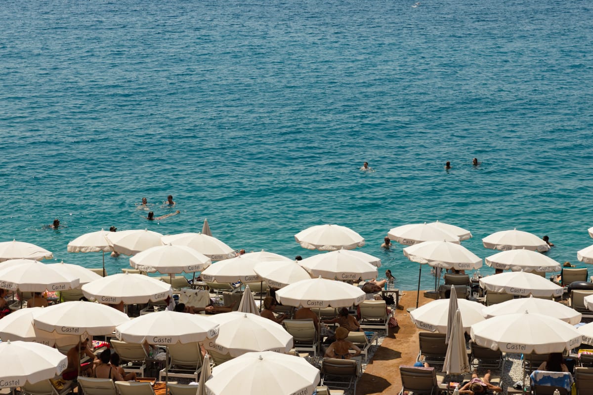 Rows of white beach umbrellas beside swimmers in turquoise water