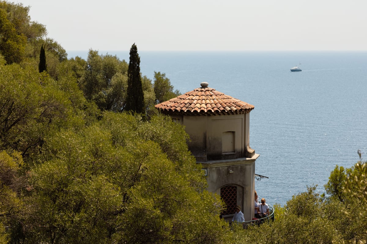 A terracotta-roofed pavilion among trees overlooking the Mediterranean Sea