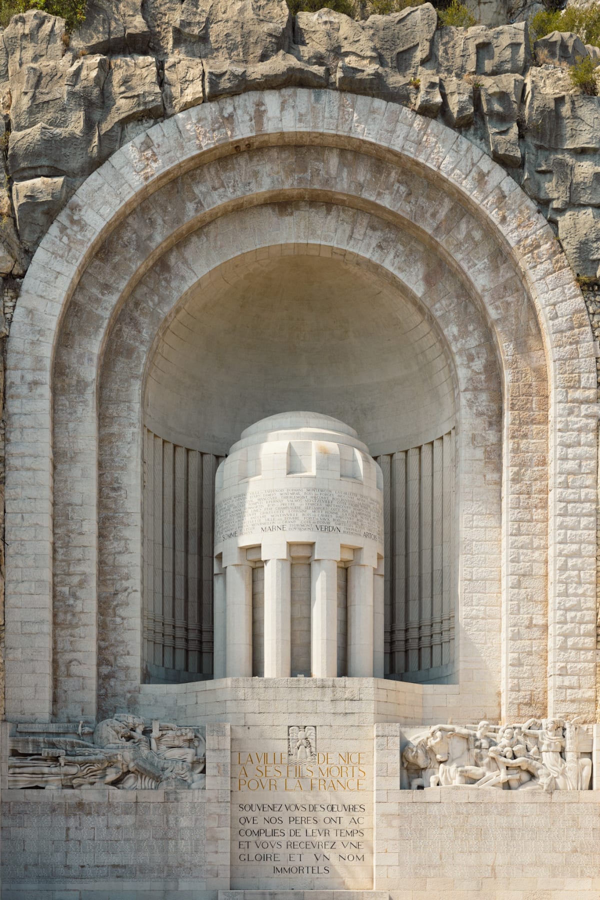 A pale stone war memorial set within a monumental rock arch