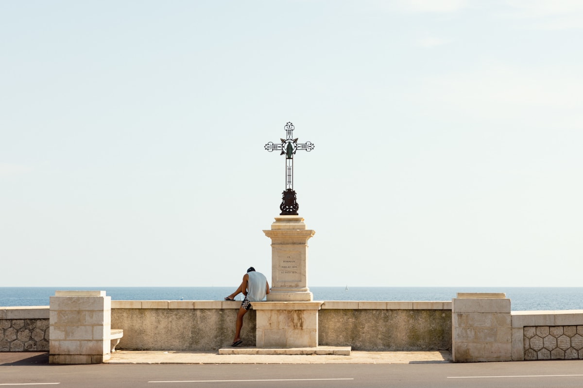 A person resting beside a coastal memorial cross overlooking the sea