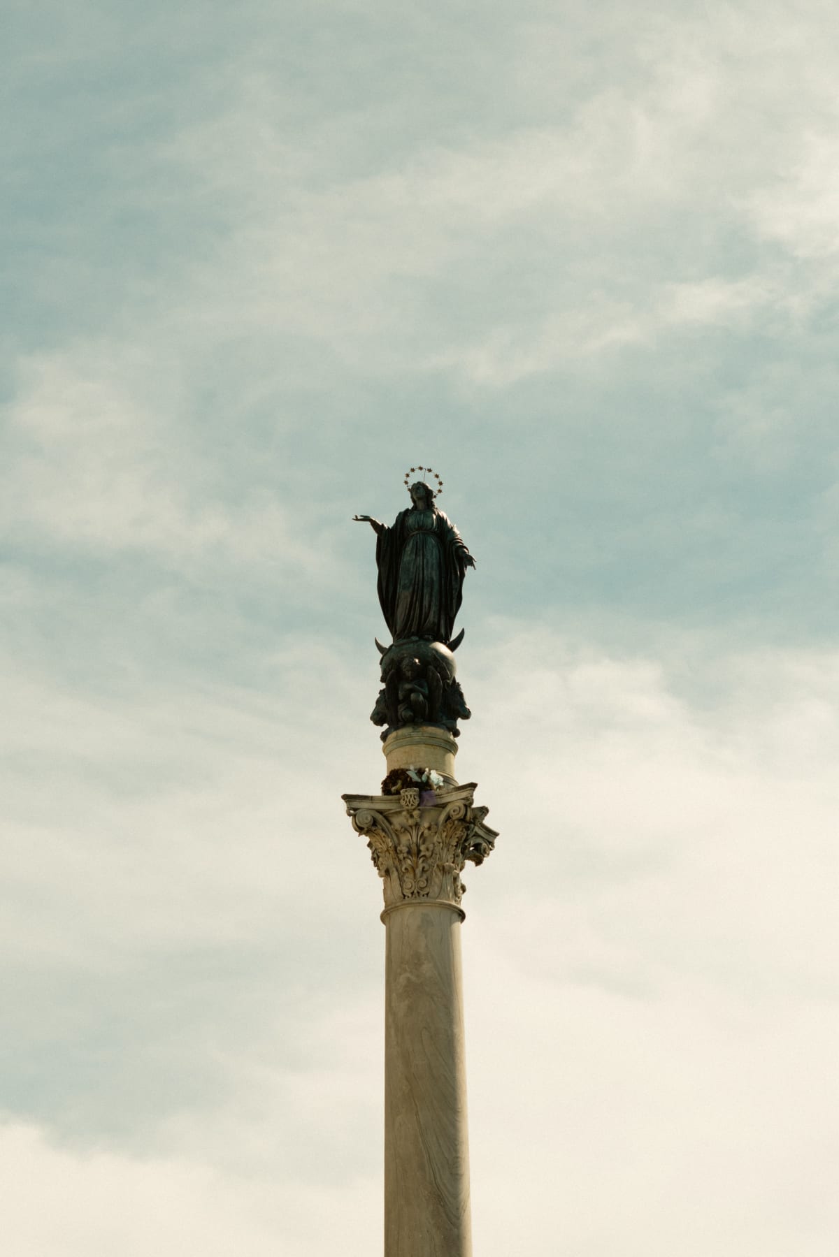A Marian statue standing atop a tall column beneath a cloudy sky