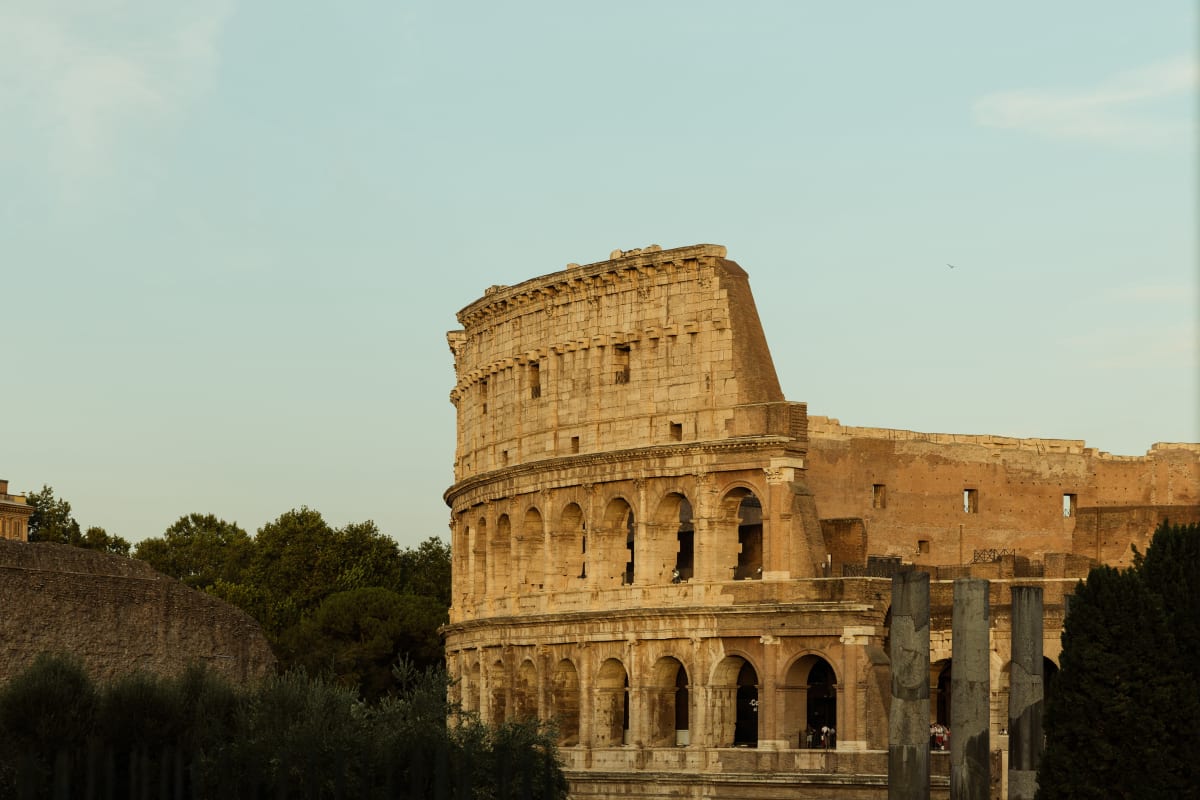 The Colosseum glowing in warm sunlight above dark greenery