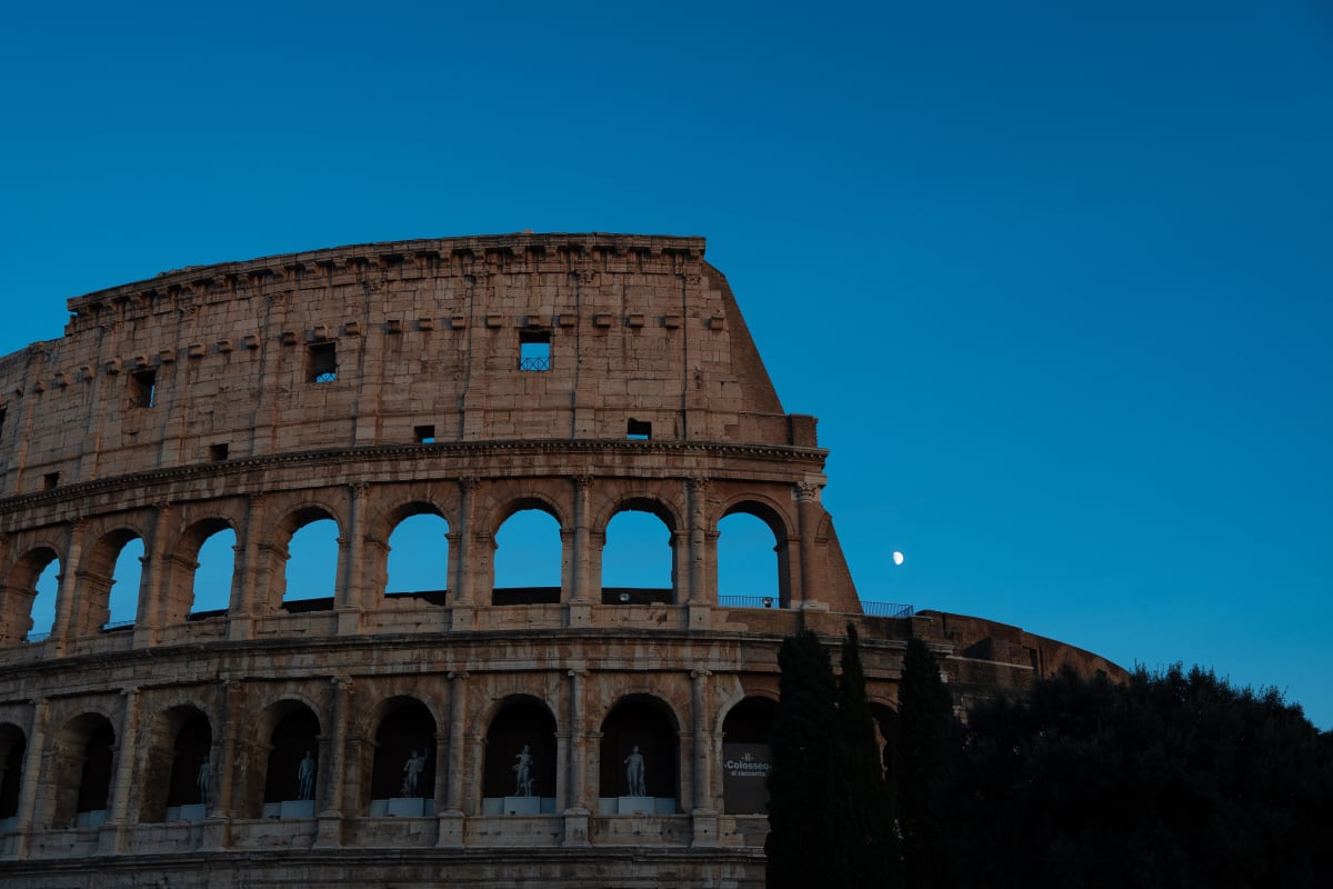 The Colosseum beneath a deep blue evening sky and a rising moon