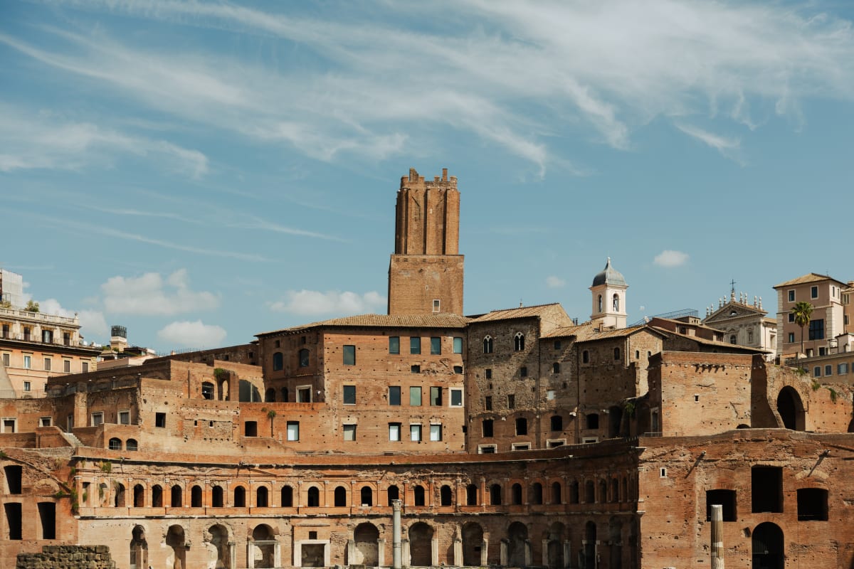 Ancient brick buildings and arcades beneath a bright Roman sky