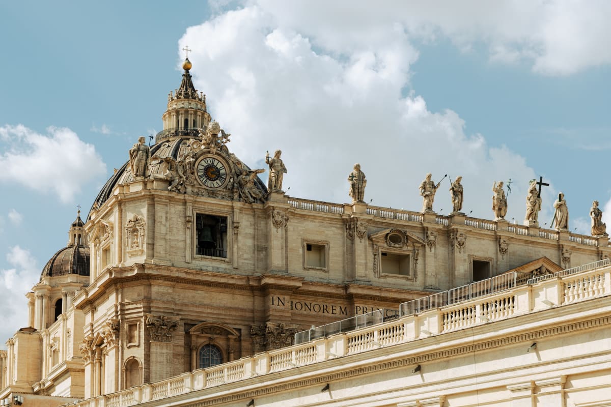 The ornate upper façade of St Peter’s Basilica beneath white clouds