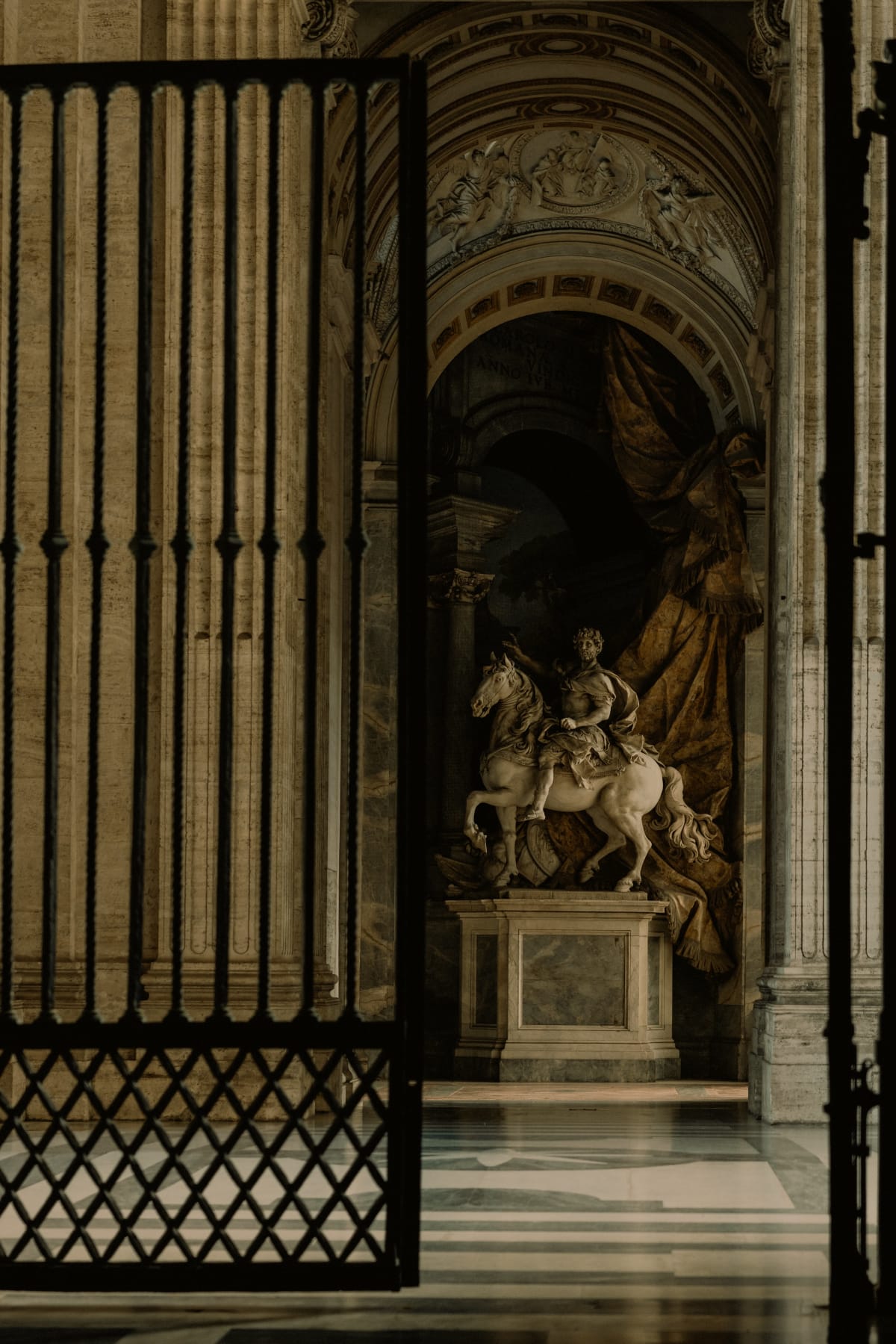 An equestrian statue framed by an ornate Vatican gate