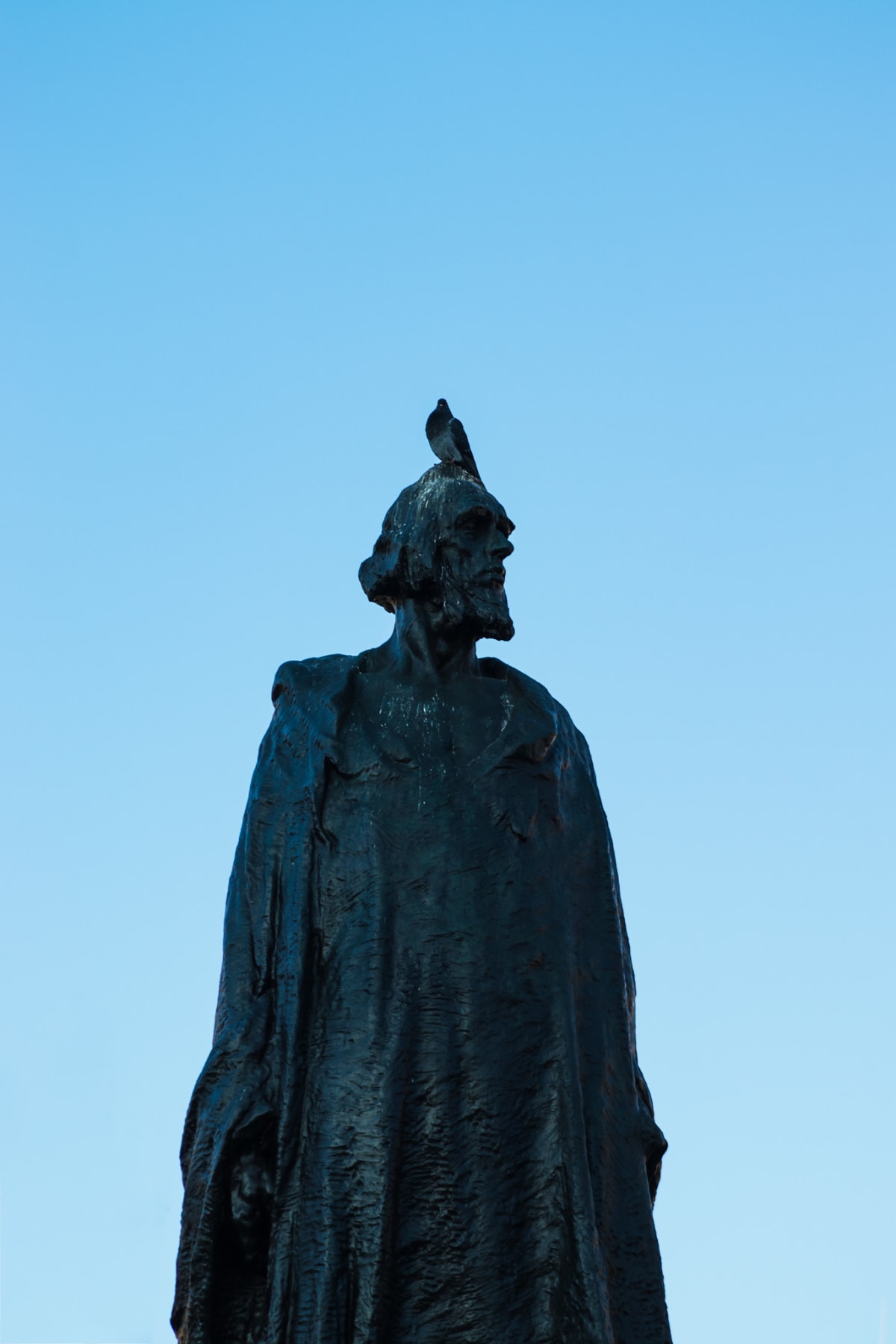A pigeon perched on the head of a weathered bronze statue