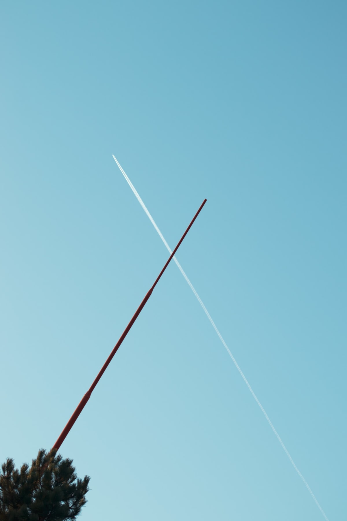 A red pole crossing a white aircraft trail in a clear blue sky