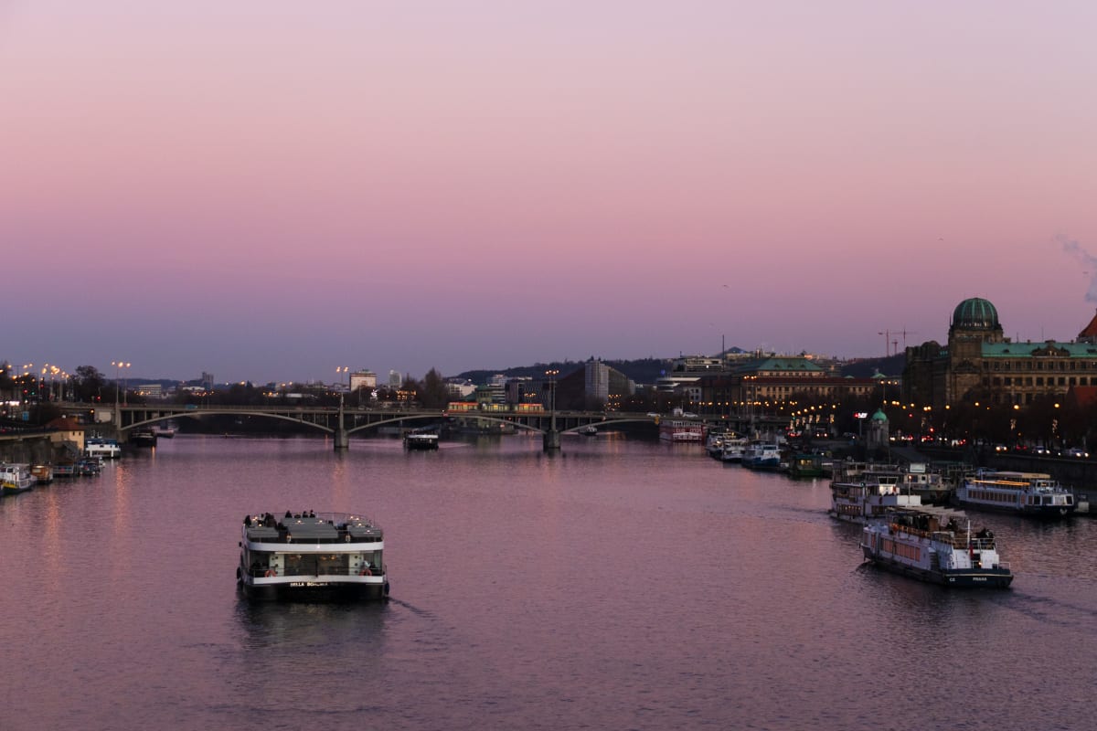 Boats crossing the Vltava beneath a pink evening sky