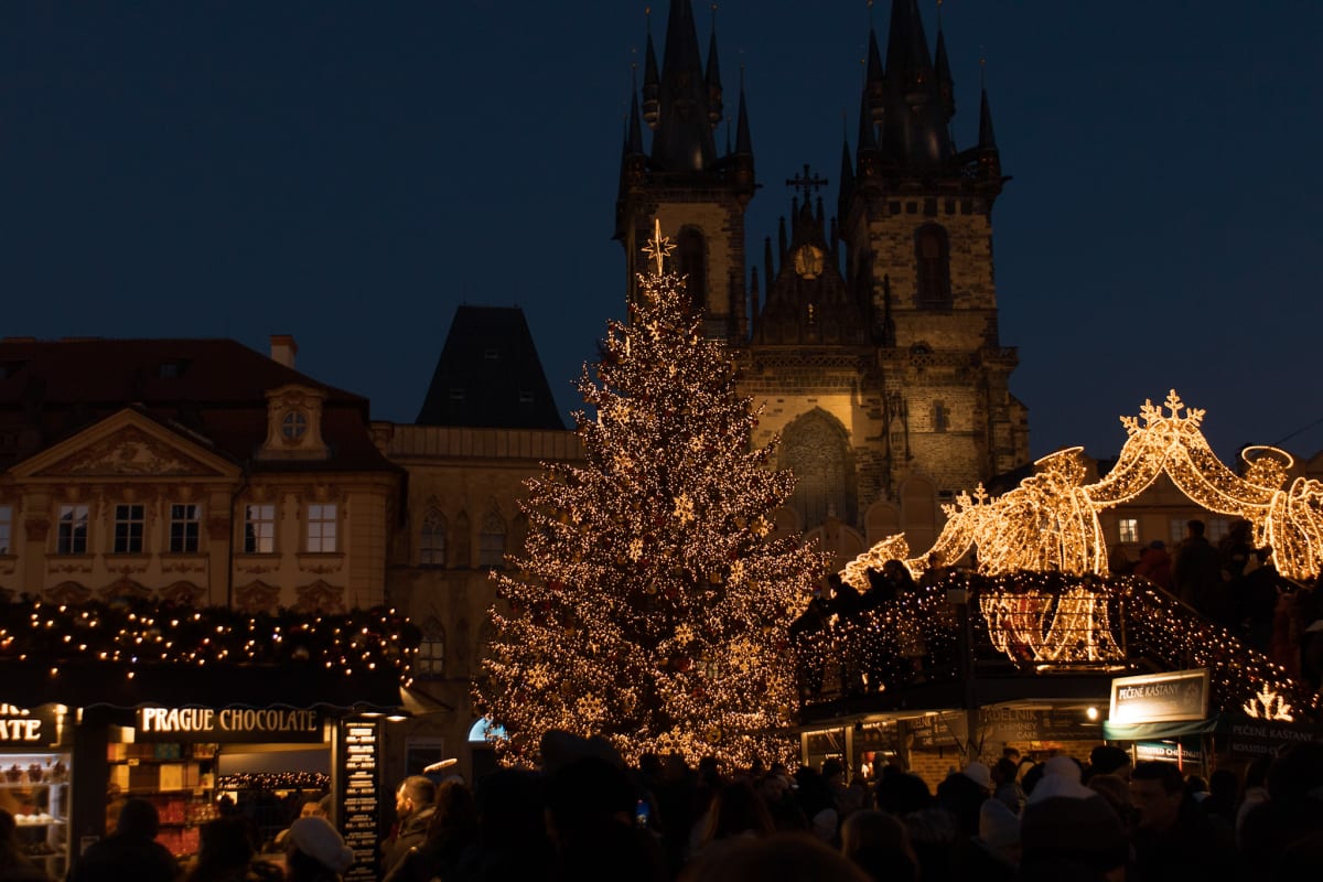A festive Prague market glowing before dark Gothic towers