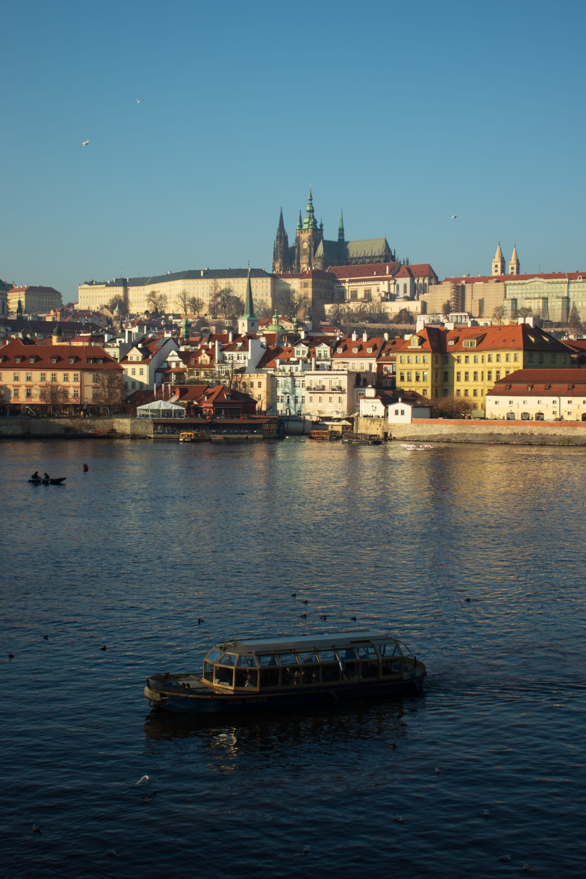 A riverboat crossing beneath Prague Castle in winter sunlight