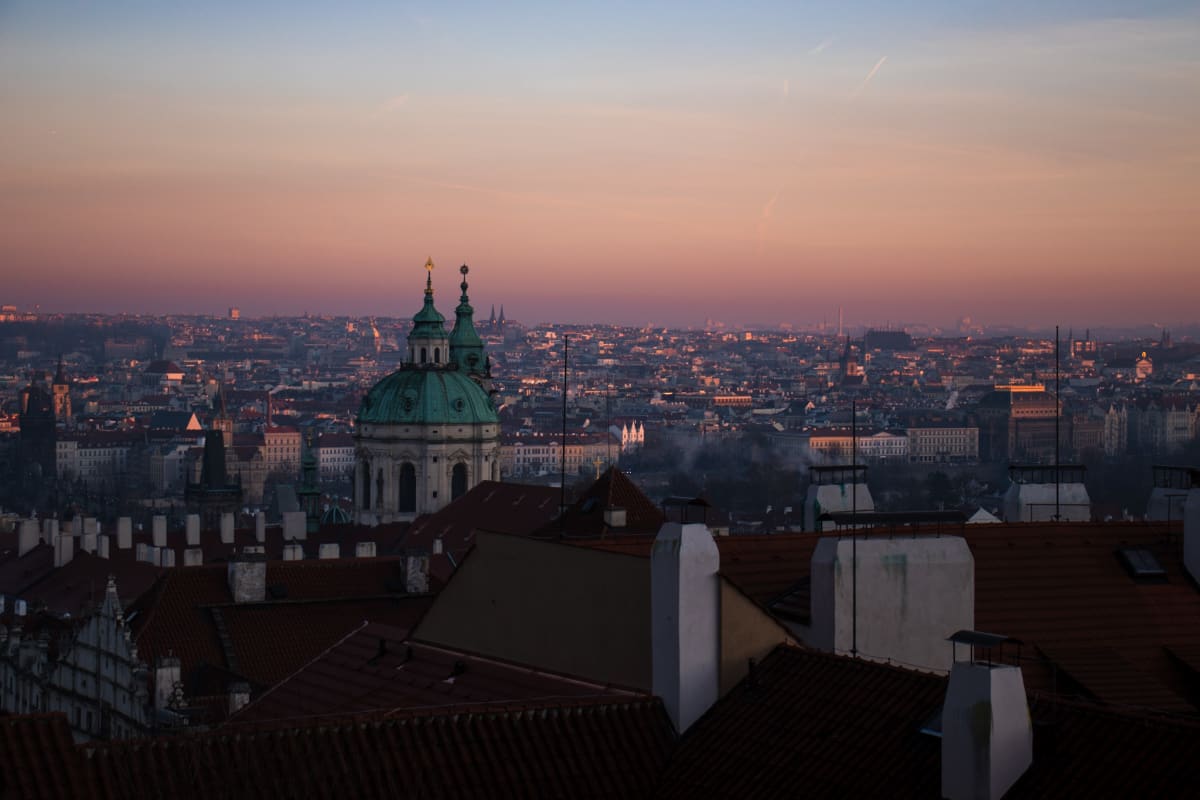 Prague rooftops and domes beneath a pastel evening sky