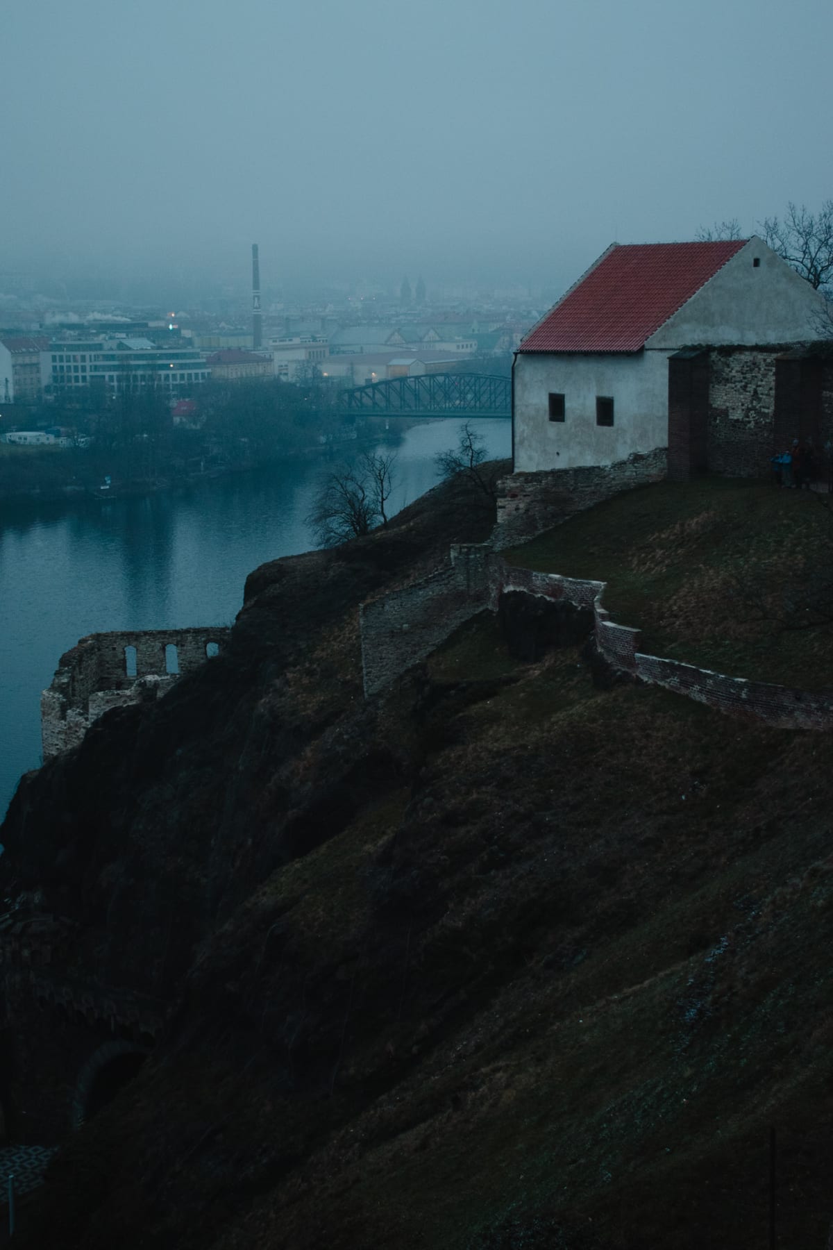 A small riverside building overlooking Prague through blue mist