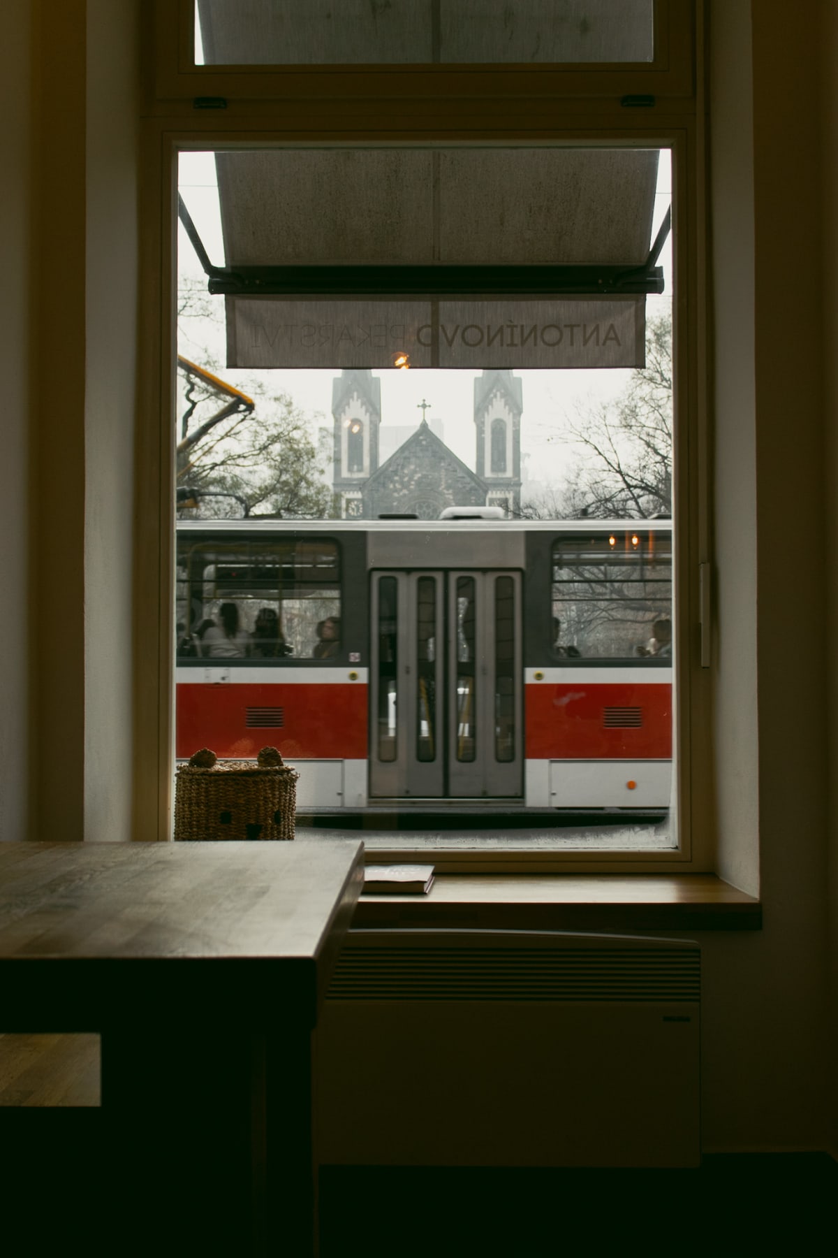A red and white tram passing a church beyond a café window