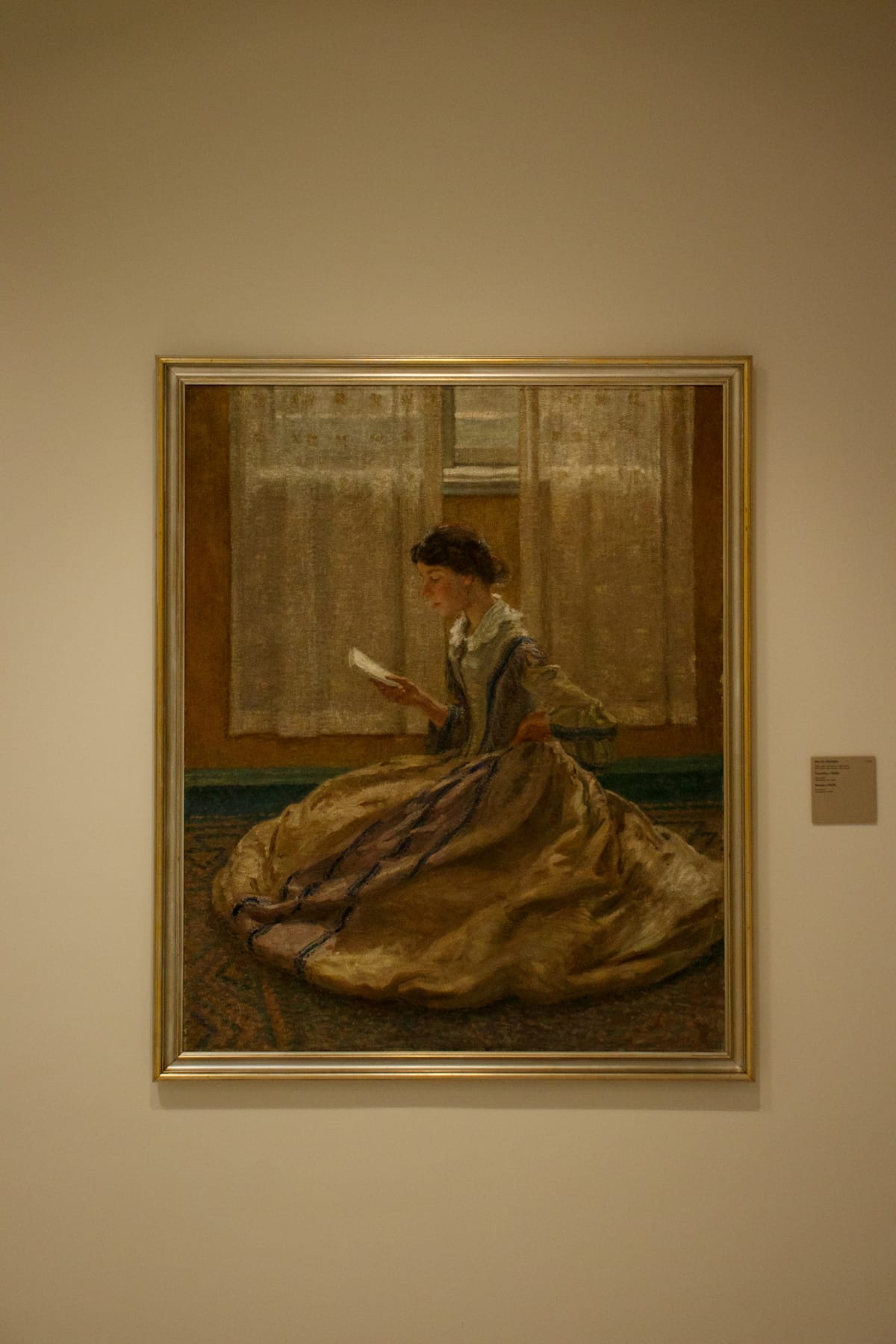 A portrait of a seated woman reading in a flowing dress