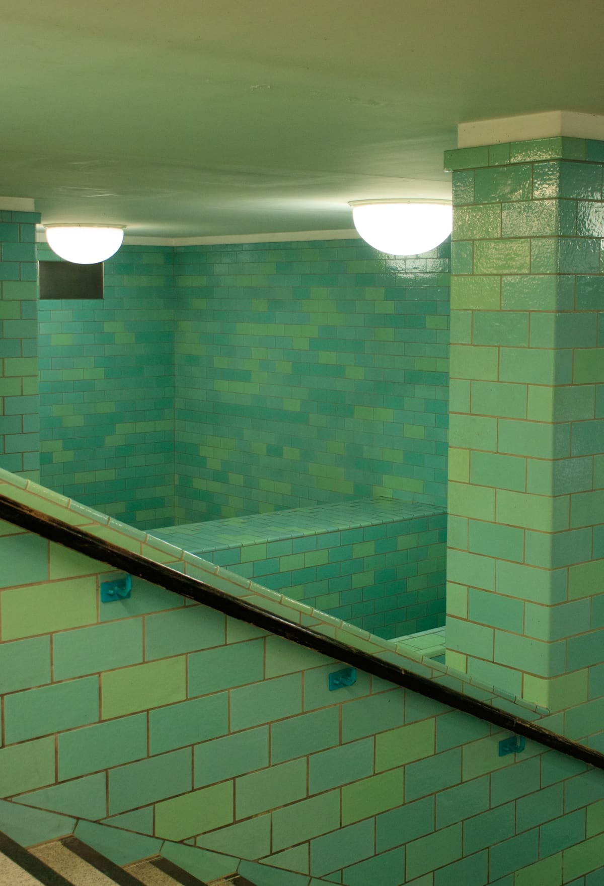 A turquoise-tiled underground stairwell lit by round lamps