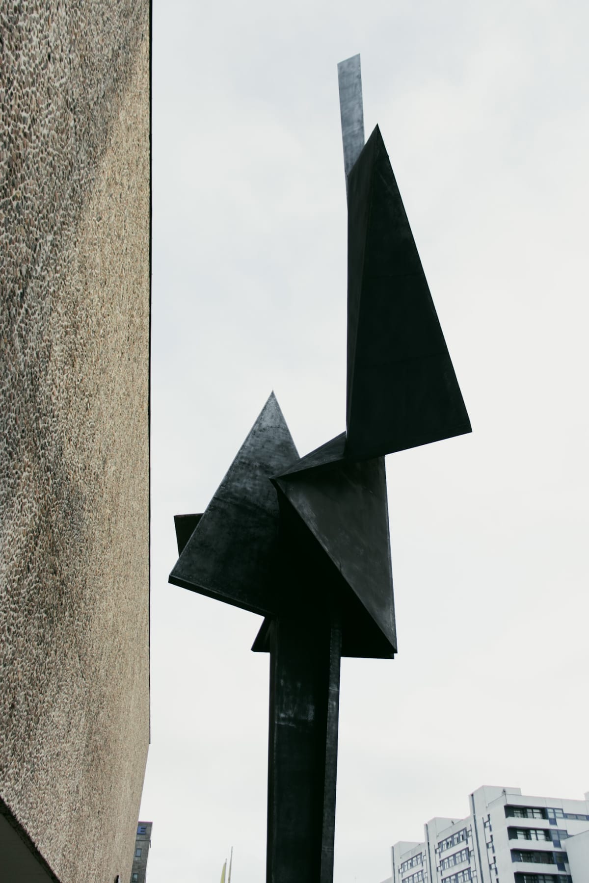 An angular black metal sculpture against an overcast sky