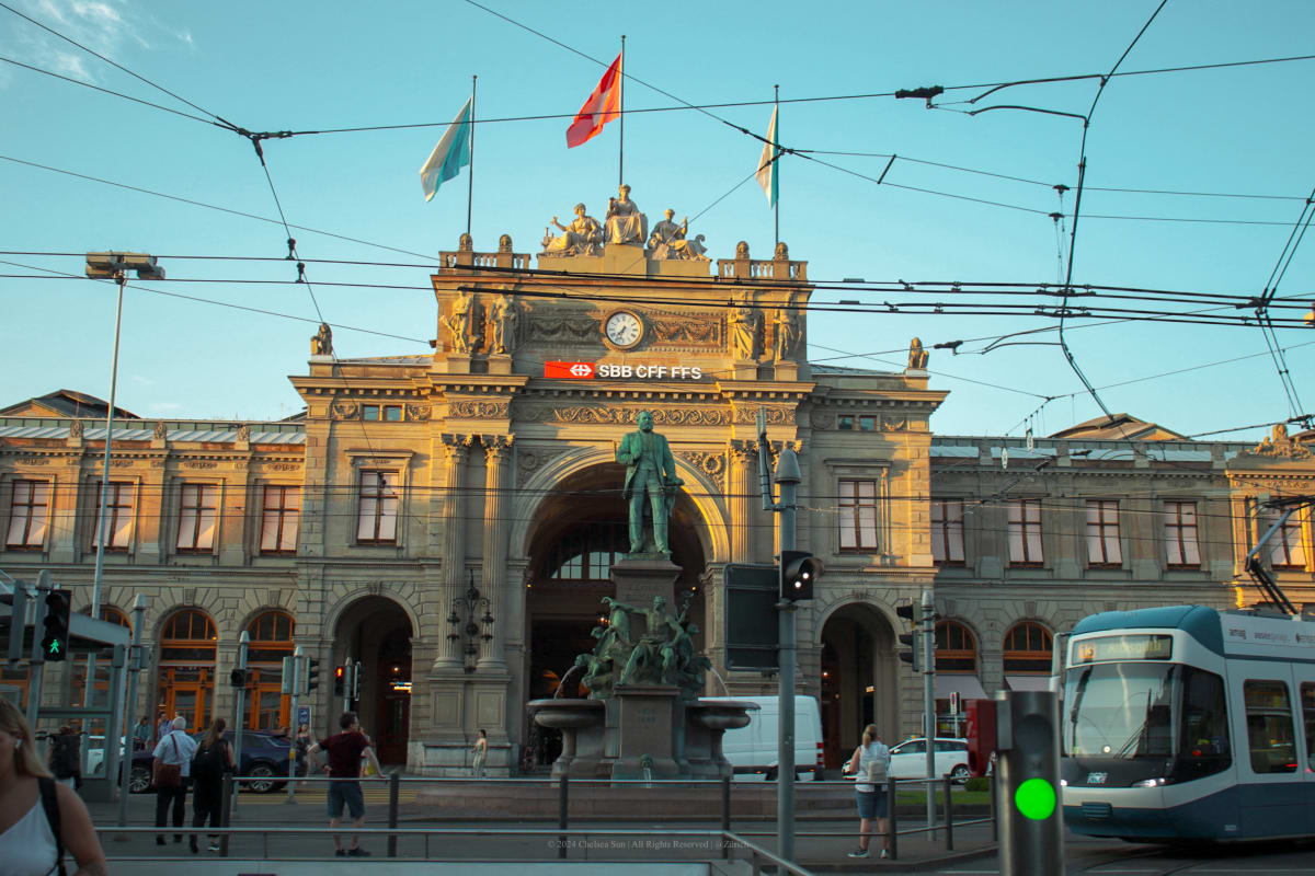 A tram passing the ornate façade of a Swiss railway station