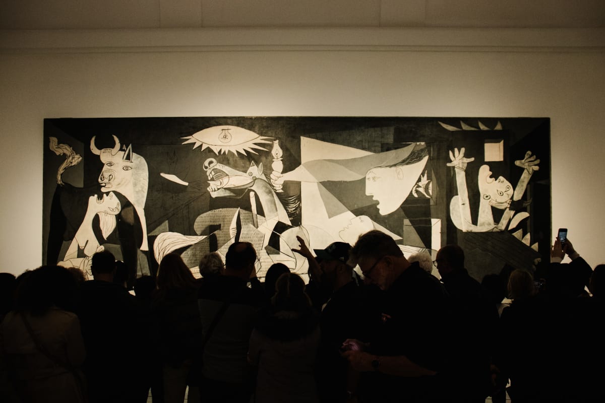 Visitors silhouetted before Picasso's Guernica in a museum