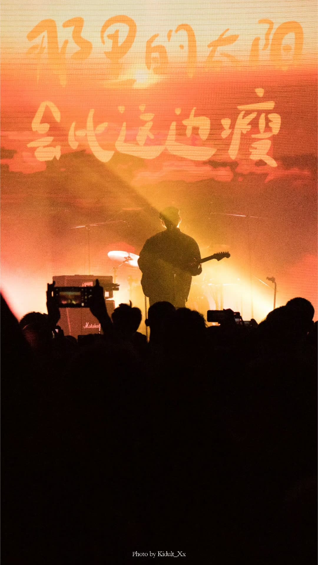 A guitarist silhouetted against a glowing orange concert backdrop