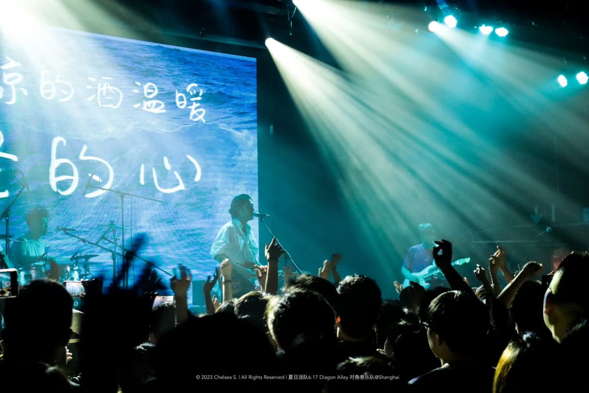 A band performing in blue light before a crowded room with raised hands