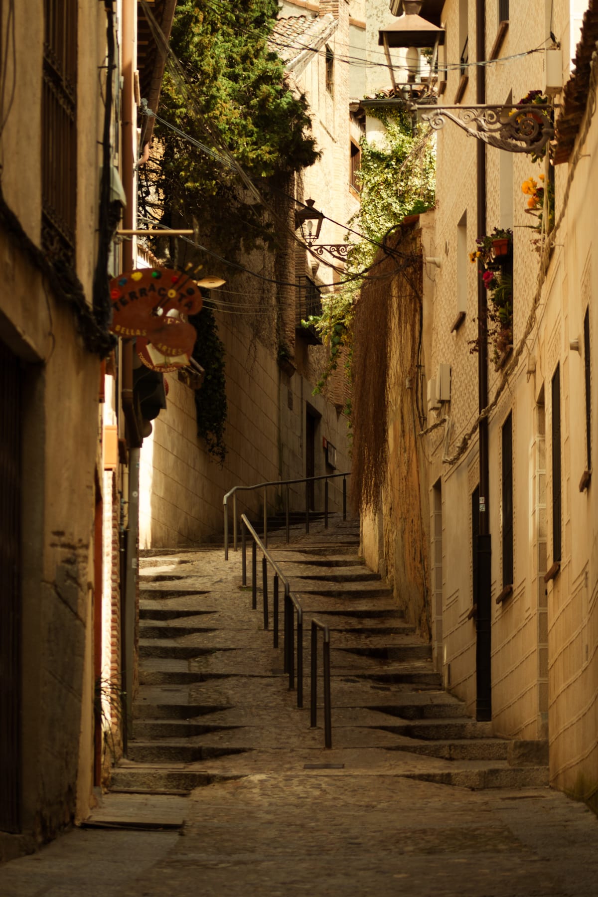A sunlit stone stairway winding between narrow Spanish buildings