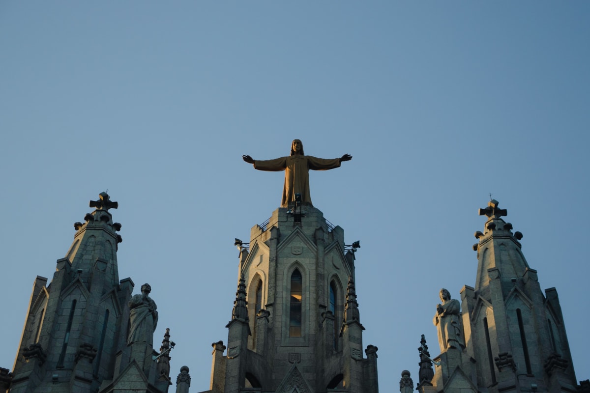 A hilltop church crowned by a statue beneath a clear blue sky