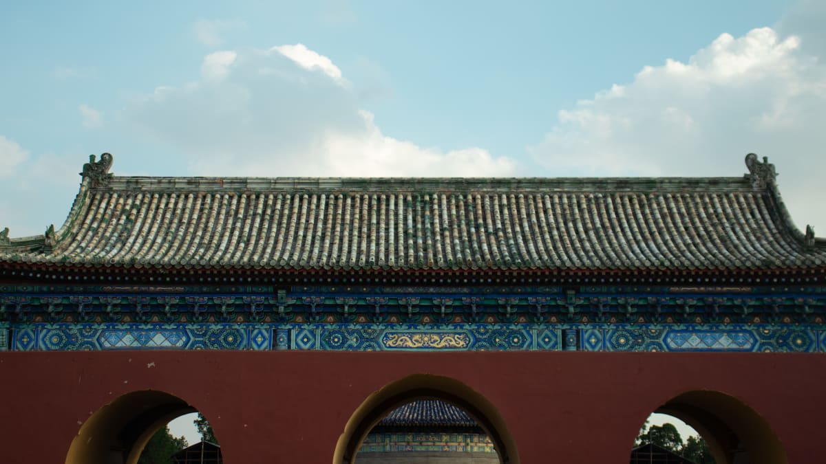 A traditional red gate and tiled roof beneath a bright blue sky
