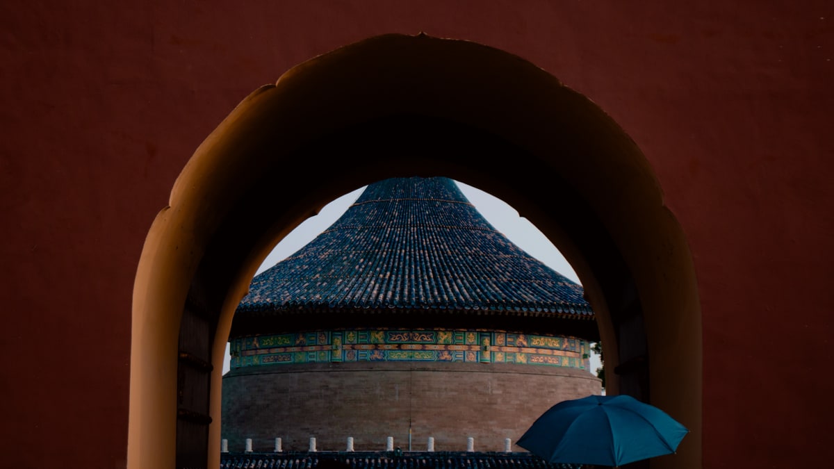 A circular temple roof framed through a red arched gateway