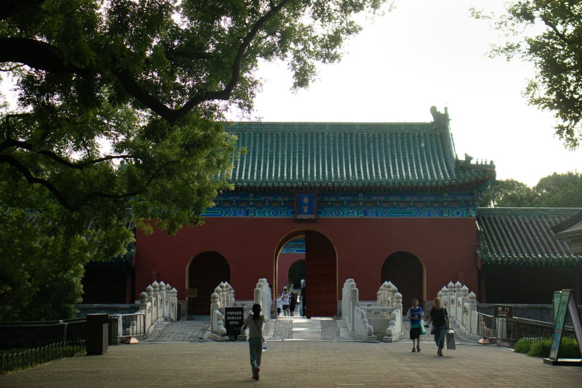 Visitors approaching a traditional gate beneath leafy branches