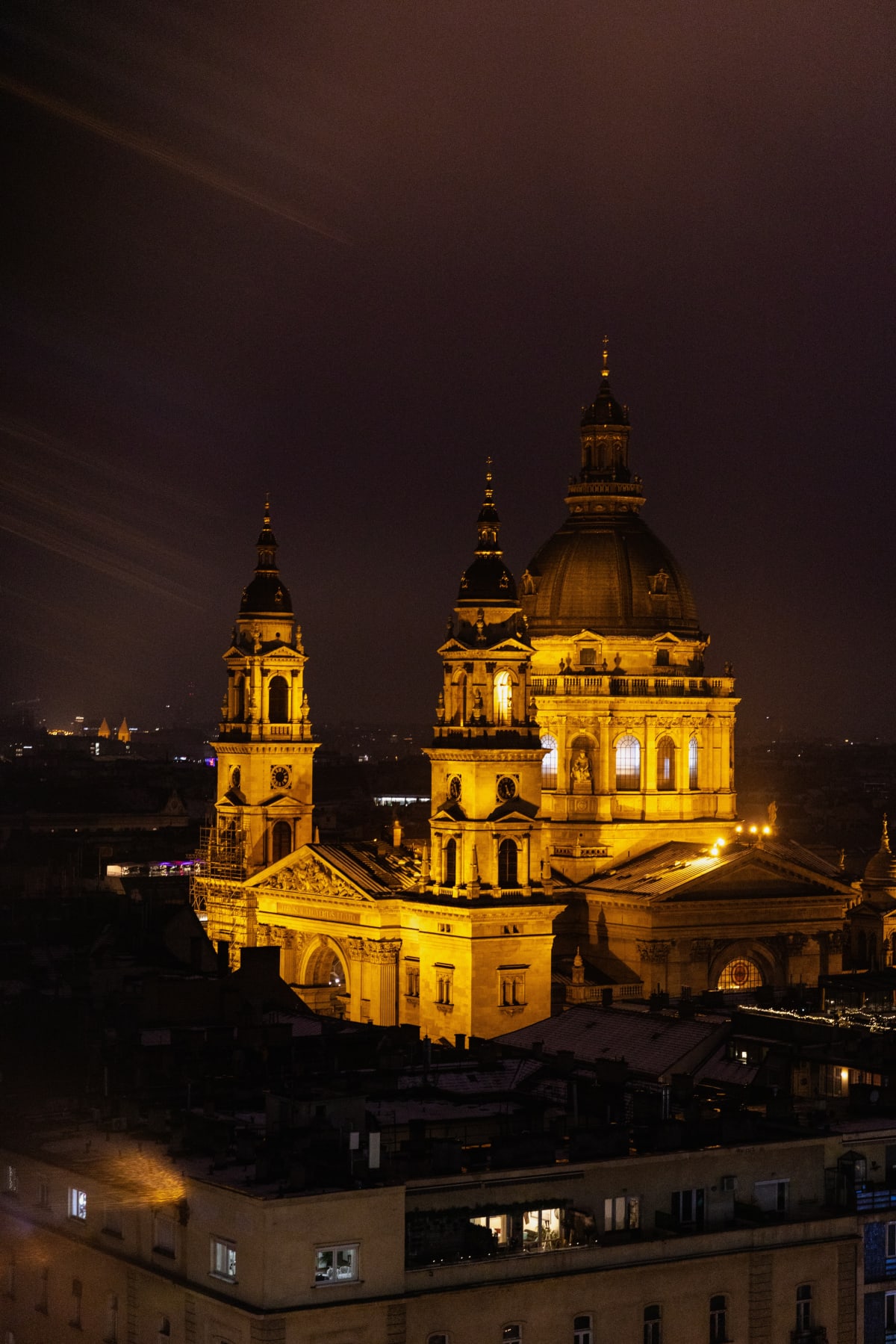 A domed basilica glowing above dark rooftops at night