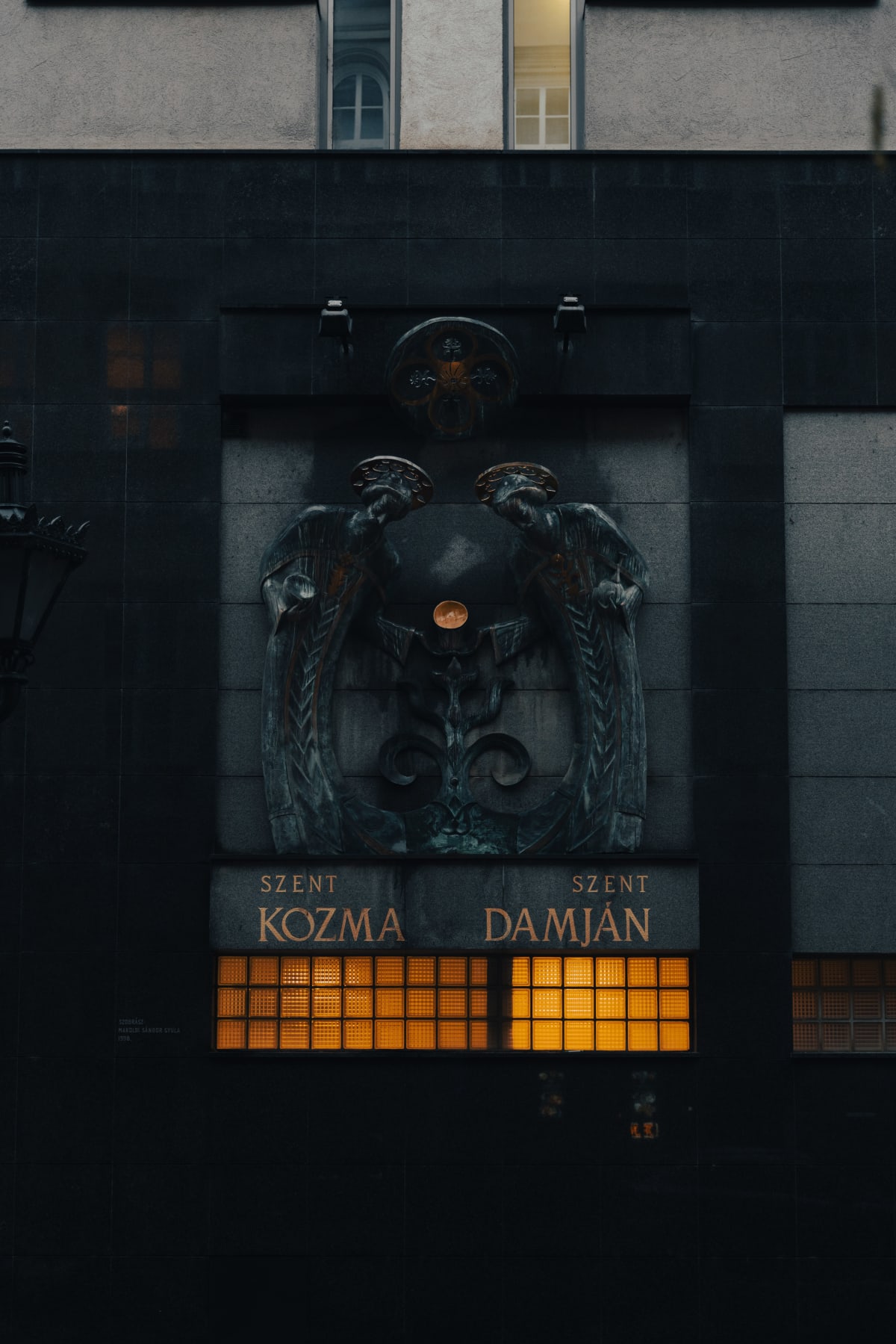 A dark stone façade with heraldic sculpture and glowing windows