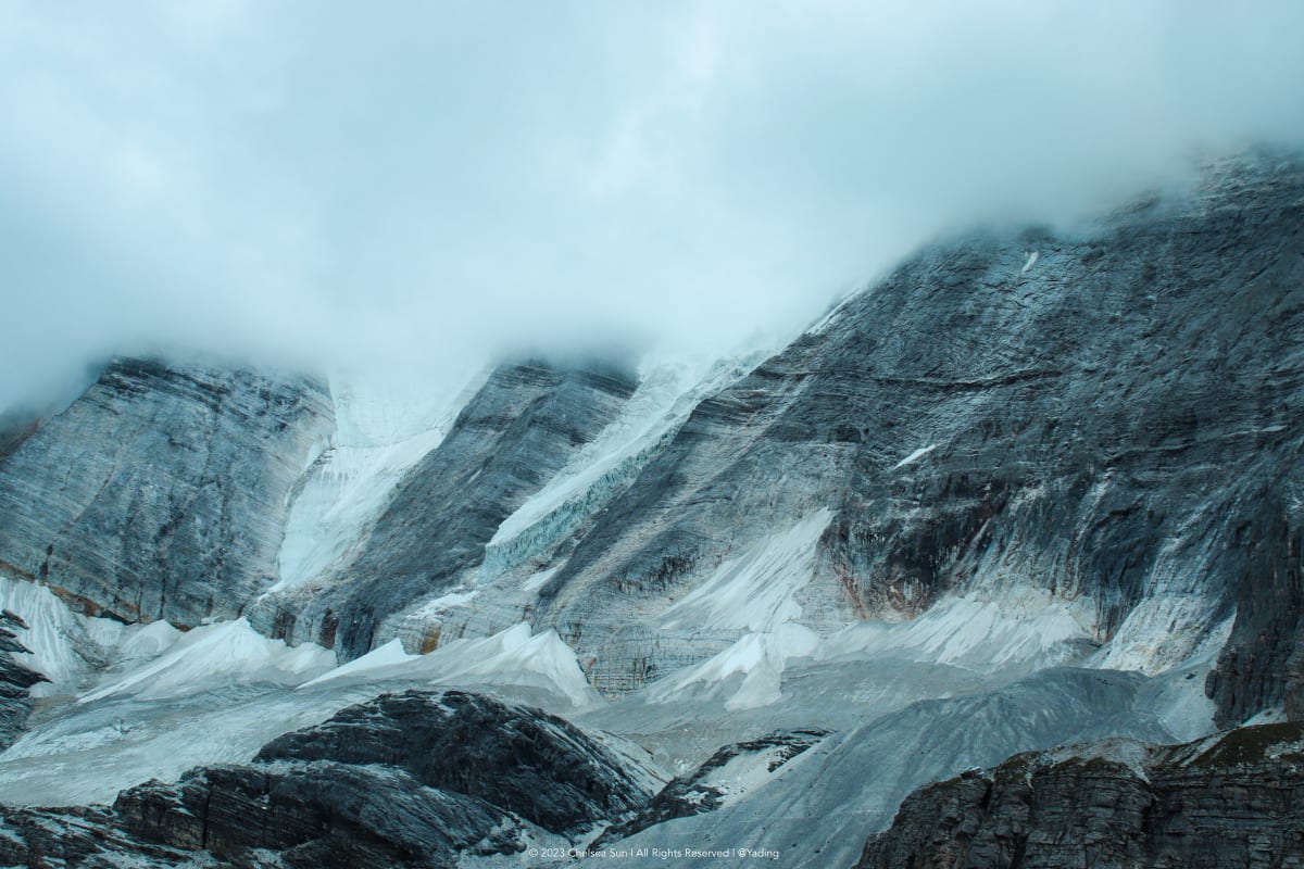 Snow-covered mountain walls disappearing into low clouds