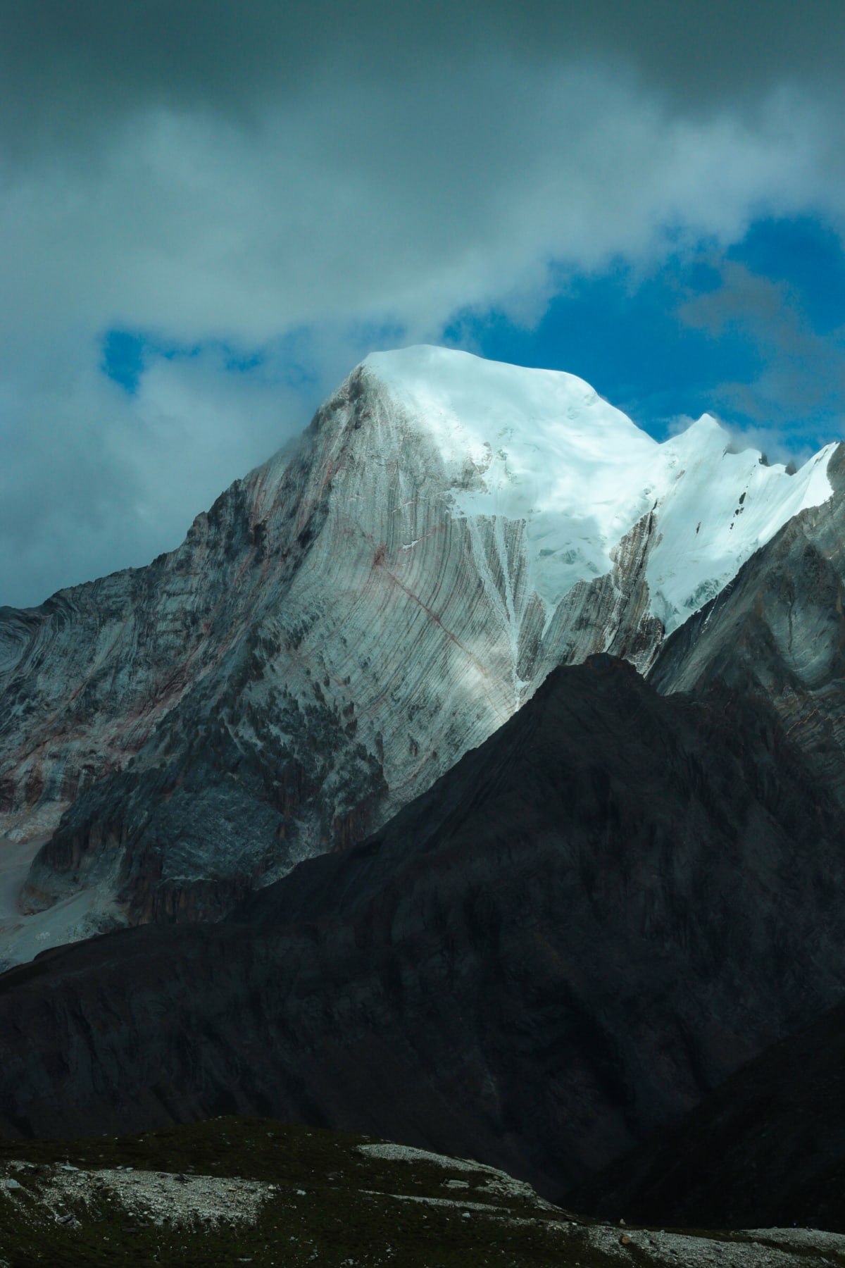 A snow-covered peak emerging between dark ridges and clouds