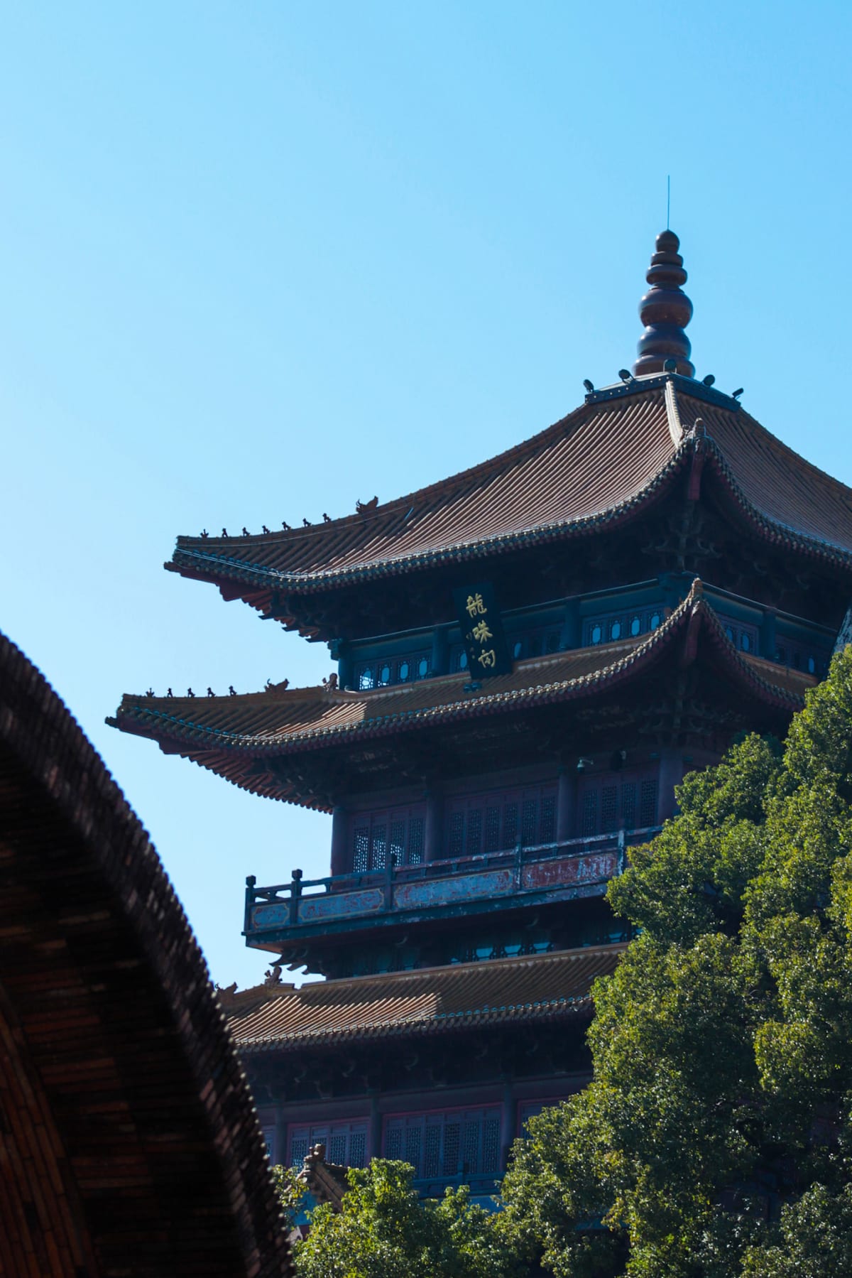 A traditional pagoda rising above green trees beneath a blue sky
