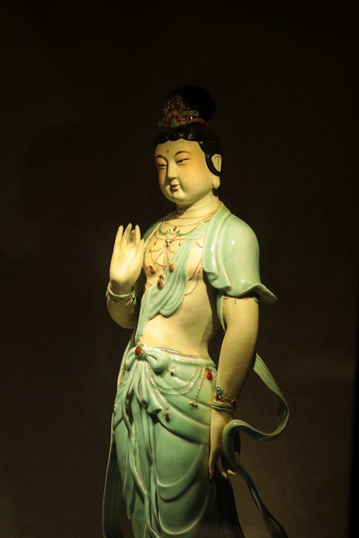 A green-glazed bodhisattva figure illuminated against a dark background