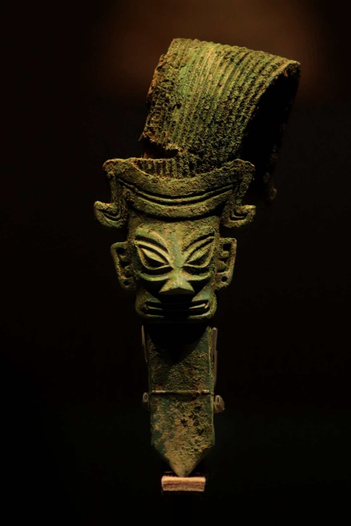 An ancient bronze mask displayed against a dark museum wall